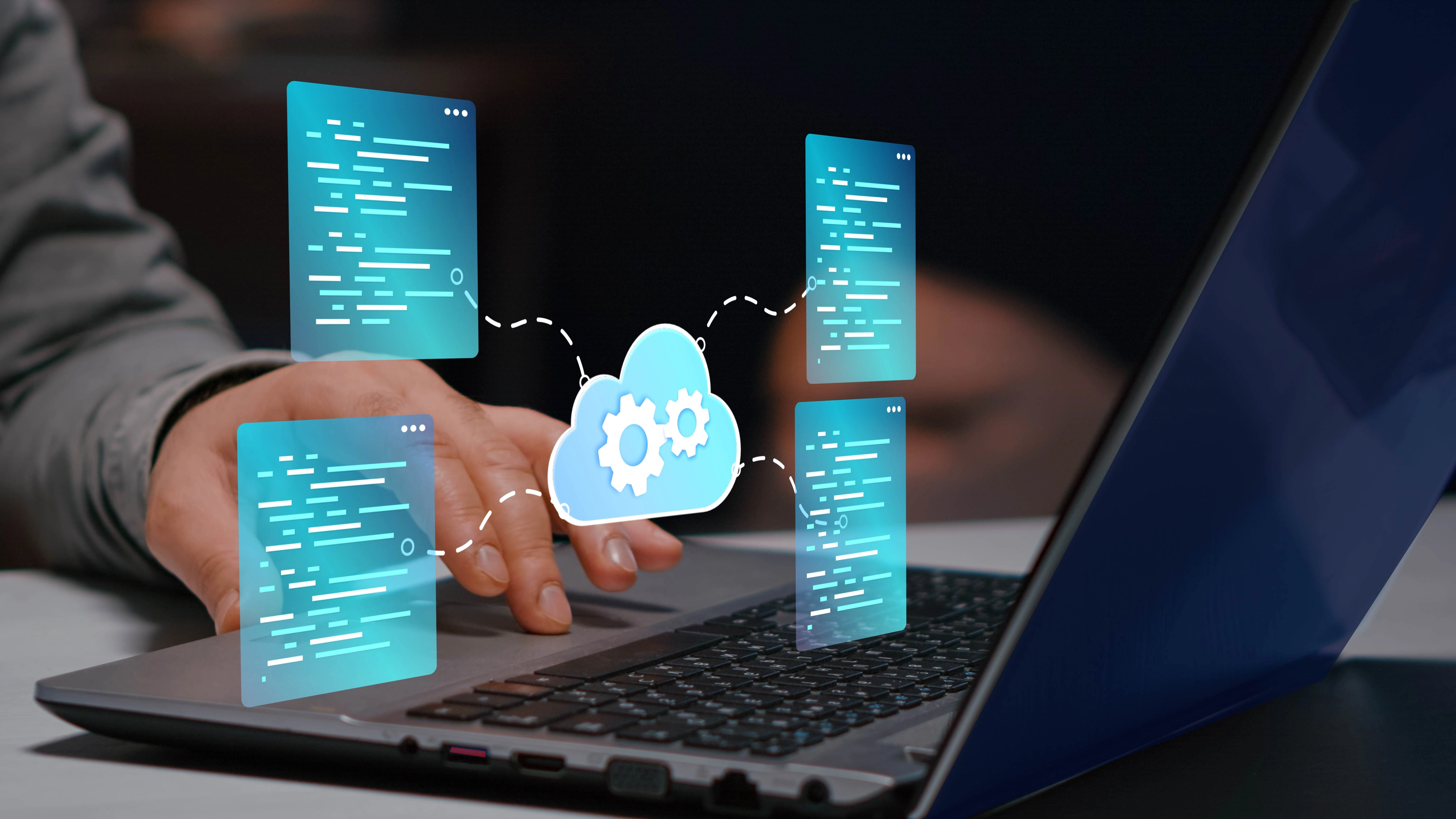 Hands typing on a laptop with blue holographic code panels and a cloud with gears, illustrating cloud computing.